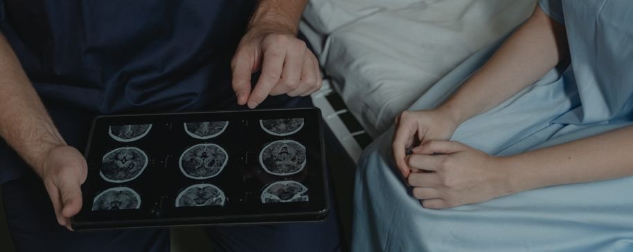 Profesional sanitario mostrando imágenes cerebrales en una tableta durante una consulta.